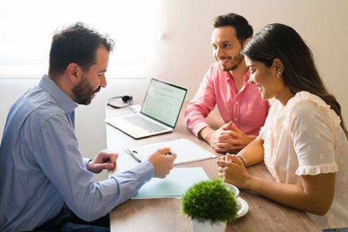 Couple sitting across a desk from a man reviewing paperwork with them in an office.